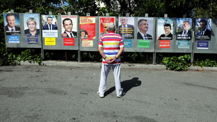 Muž se upřeně dívá na plakáty jednotlivých prezidentských kandidátů