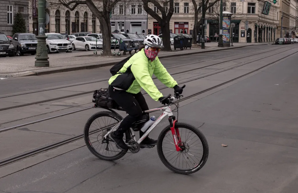 S nošením ochrany dýchacích cest si musí poradit i cyklisté. Na fotografii projíždí muž poblíž mostu Legií