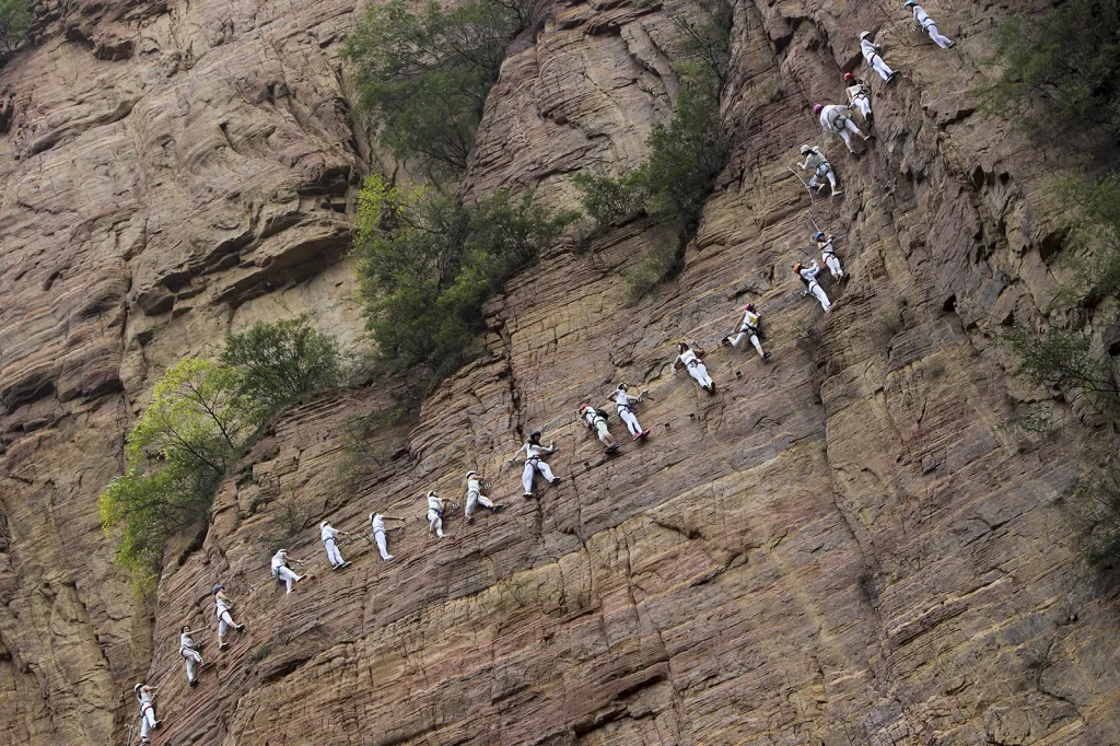 Lidé přidržující se lana zdolávají skalní stěnu v pohoří Qingyao v čínské provincii Henan