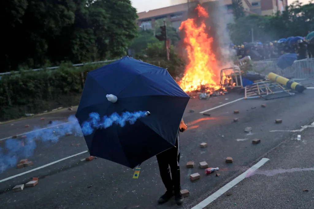 Odpůrce vlády se kryje pod deštníkem během konfrontace policistů s demonstranty v Ša Tchi v Hongkongu