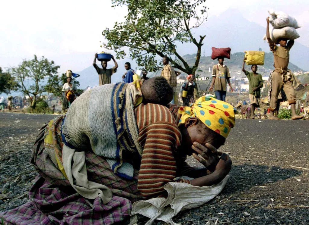 Žena z Rwandy kolabuje i se svým dítětem na zádech vedle silnice spojující uprchlický tábor Kibumba s městem Goma 28. července 1994. Úředníci říkali, že denně zemřelo v okolí táborů 1800 lidí