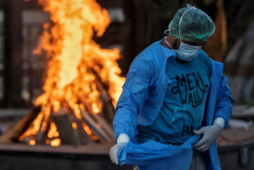 Řidič ambulance Mohammad Aamir Khan si mění ochranný oblek během kremace jedné z obětí koronaviru. Nové Dillí, Indie, 2020