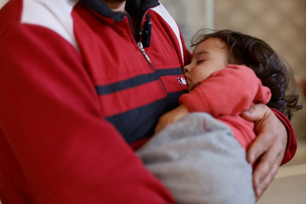 Rodič drží svou spící dceru v náručí. Syrská rodina žije ve stanovém městě v tureckém Mersinu. Tábor pojme více než dvě stě lidí