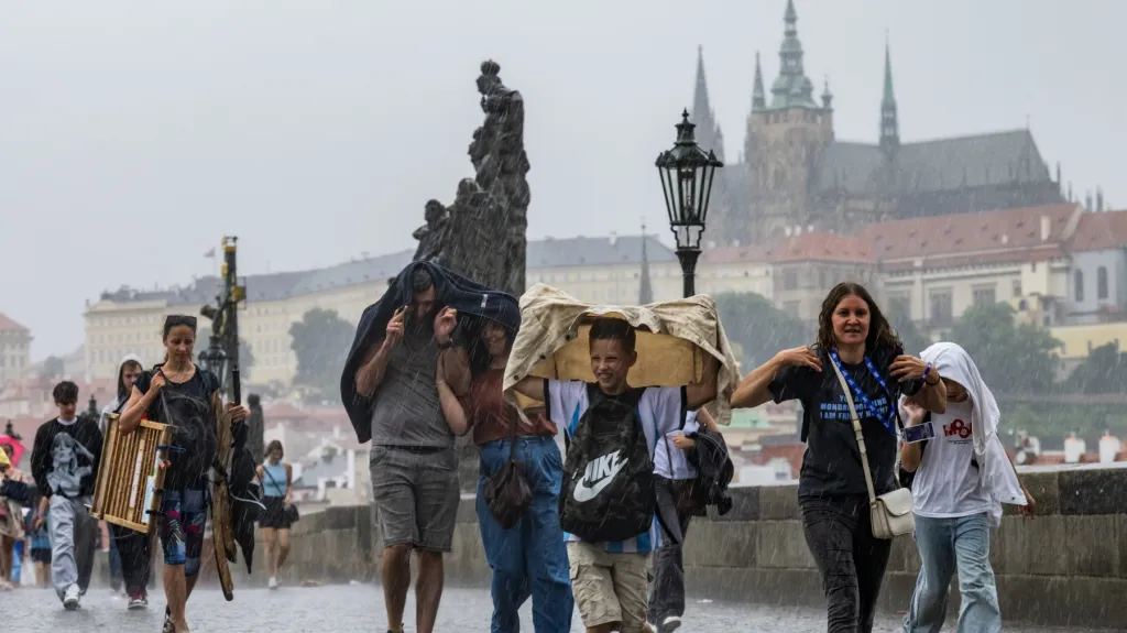 Lidé na Karlově mostě v Praze během silného deště