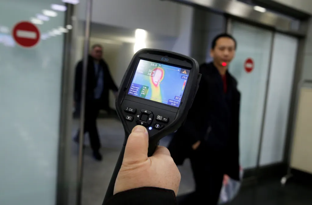Pracovník letiště v kazašském Almaty měří teplotu pasažérům, kteří přicestovali z Číny
