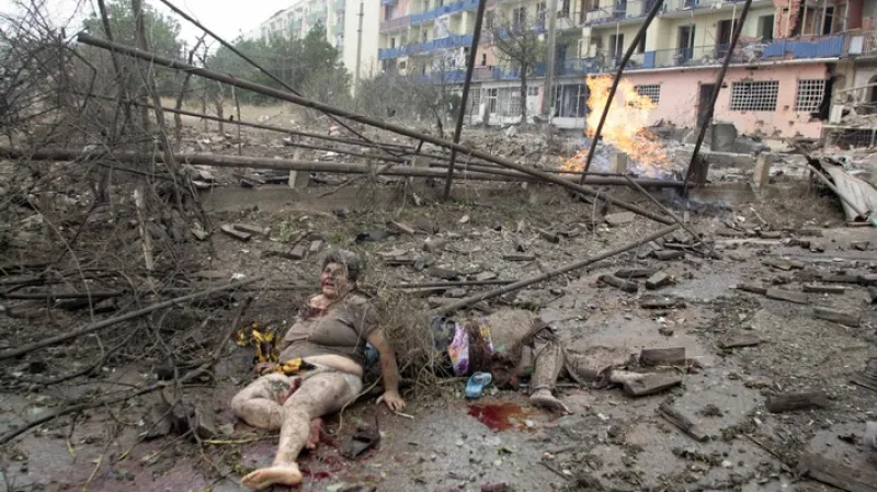 Zraněná žena leží před troskami vybombardovaného domu v gruzínském městě Gori.