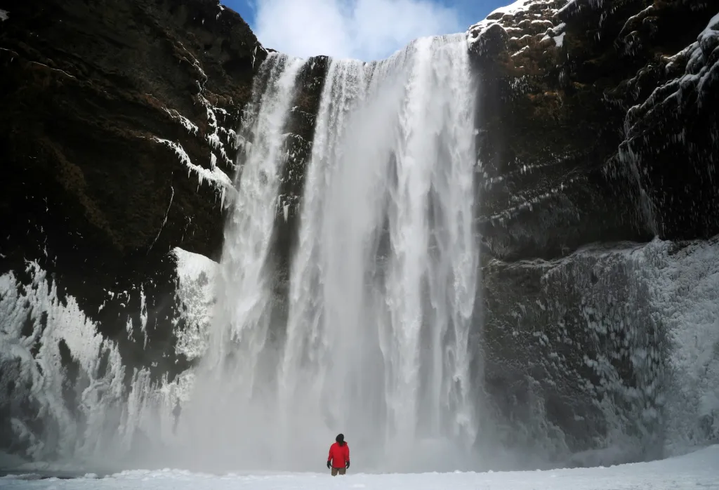 Turista na Islandu obdivuje vodopád ve Skogaru