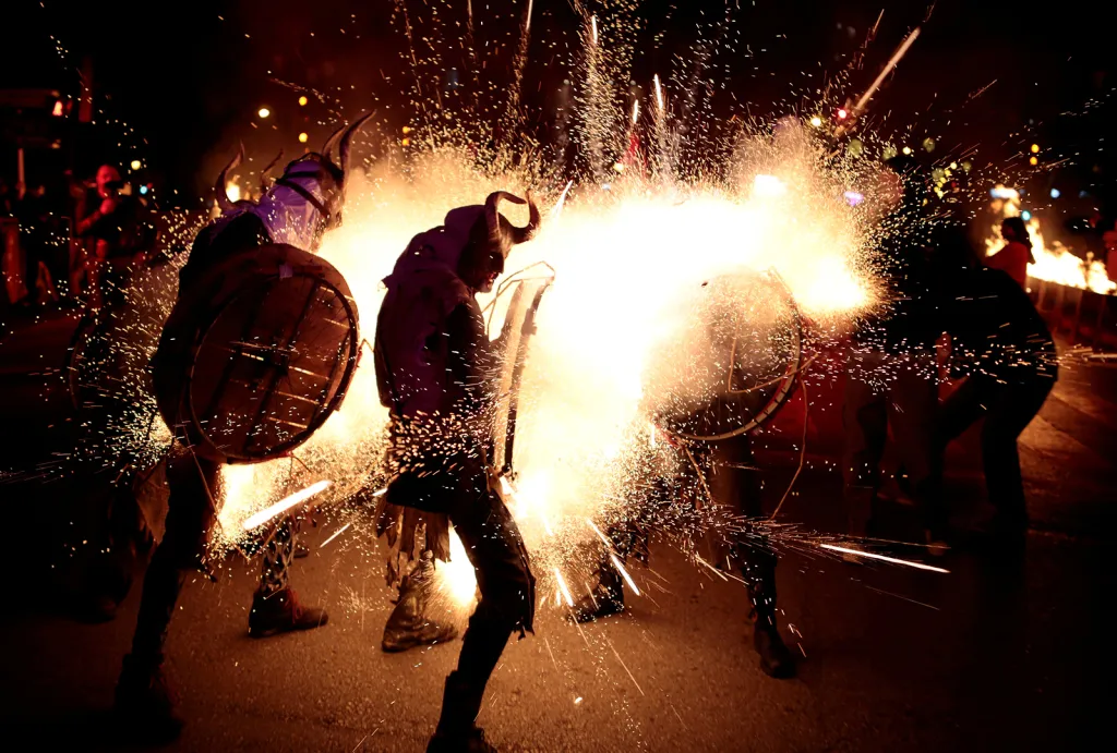 Španělský tradiční svátek Correfocs a účastníci průvodu převlečení za ďábly tančí mezi rachejtlemi