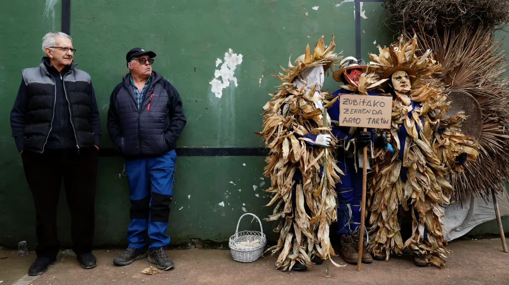 Muži stojí vedle vesničanů oblečených do kukuřičných slupek a listí