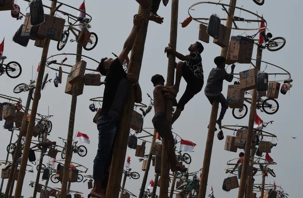 V Indonésii muži soutěží v lezení po namazaných tyčích. Odměnou jsou jim ceny zavěšené na koncích stožárů