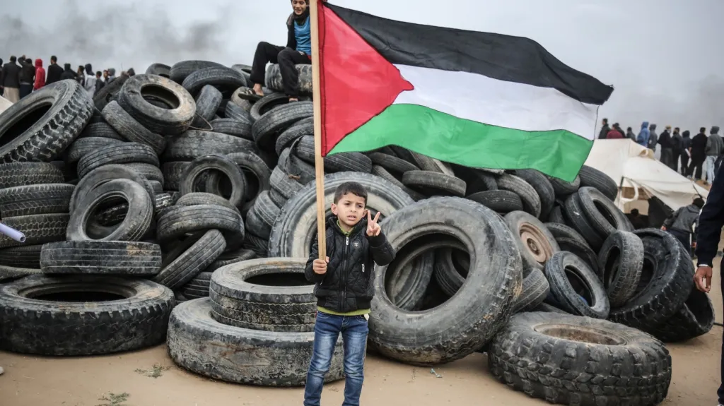 Chlapec s palestinskou vlajkou u hromady navozených pneumatik v rámci protestů na hranici Pásma Gazy s Izraelem