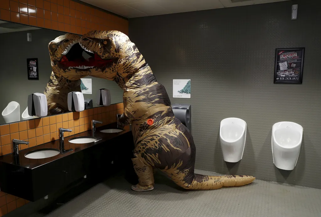 Účastník londýnského festivalu popkultury London Comic Con v masce tyranosaura Rexe na veřejných toaletách