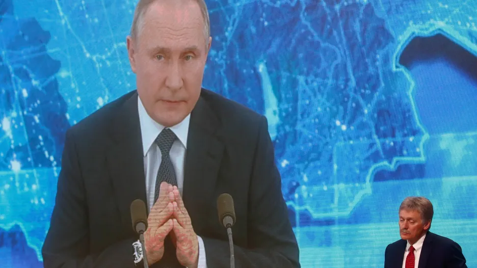 Šéf Kremlu Putin na obrazovce přenosu z tiskové konference, v rohu mluvčí Peskov