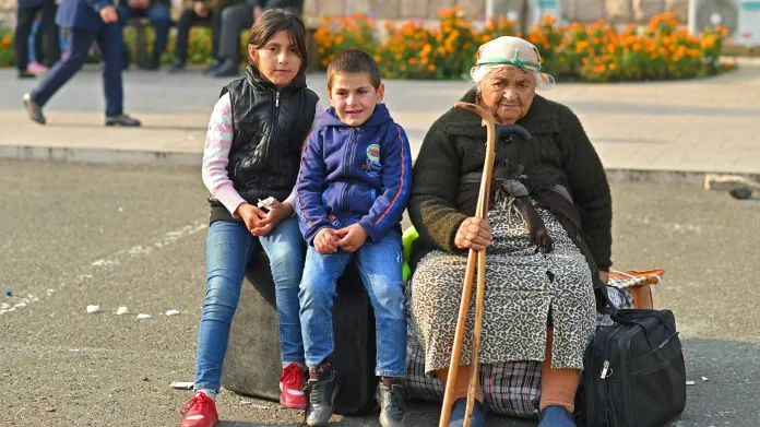 Starší žena s dětmi čeká v centru Stěpanakertu na autobus do Arménie
