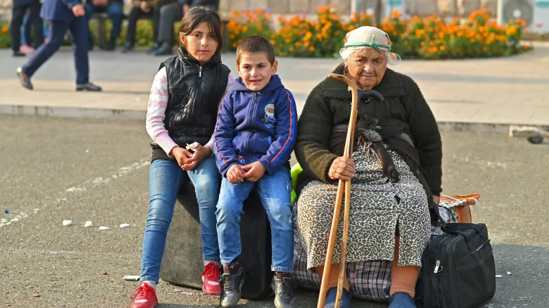 Starší žena s dětmi čeká v centru Stěpanakertu na autobus do Arménie