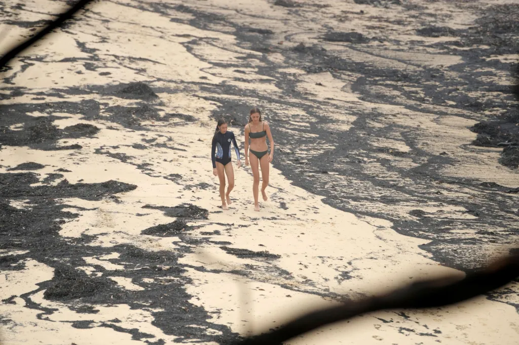 Dívky se procházejí po pláži, která je pokrytá popelem. Ten vznikl během dlouhodobých požárů v Austrálii. Fotografie je z pláže Mallacota