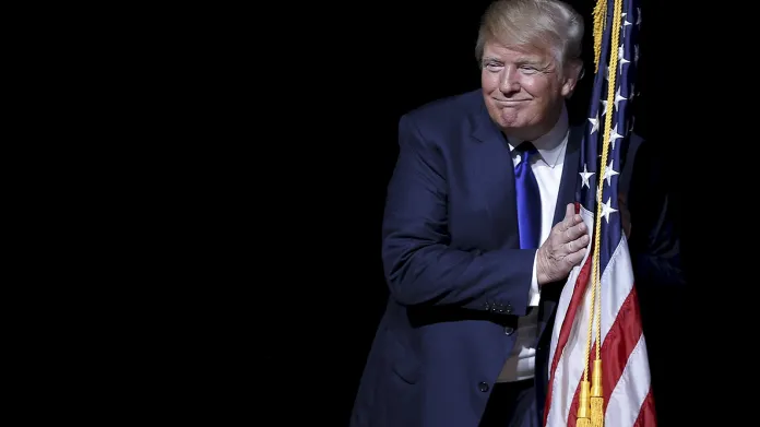 Republikánský kandidát Trump v objetí s americkou vlajkou před svým vstoupením na radnici ve městě Derry ve státě New Hampshire