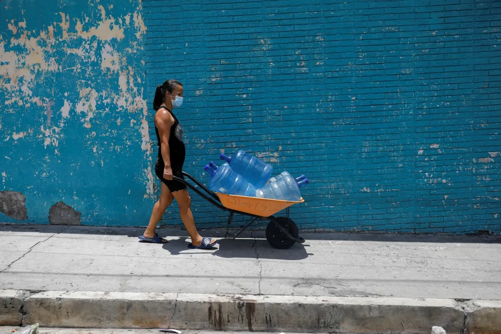 Žena tlačí vozík s plastovými nádobami naplněnými pitnou vodou v městě Soyapango v Salvadoru, poté co selhala vodovodní síť. Ta byla mimo provoz přes měsíc, což lidem v oblasti způsobila nemalé komplikace