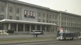 Doprava v ulicích Pchjongjangu a portréty korejských vůdců na úřední budově