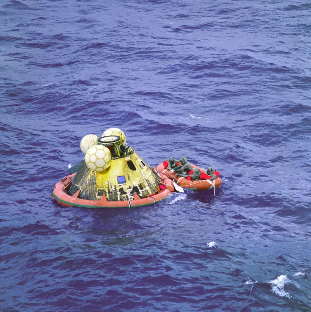 Posádka Apolla 11 a člen podmořského týmu, poručík Clancy Hatleberg, jsou oblečení v izolačním oděvu v blízkosti velitelského modulu Columbia během čekání na vyzvednutí na palubu lodi USS Hornet v Tichém oceánu jihozápadně od Havaje dne 24. července 1969