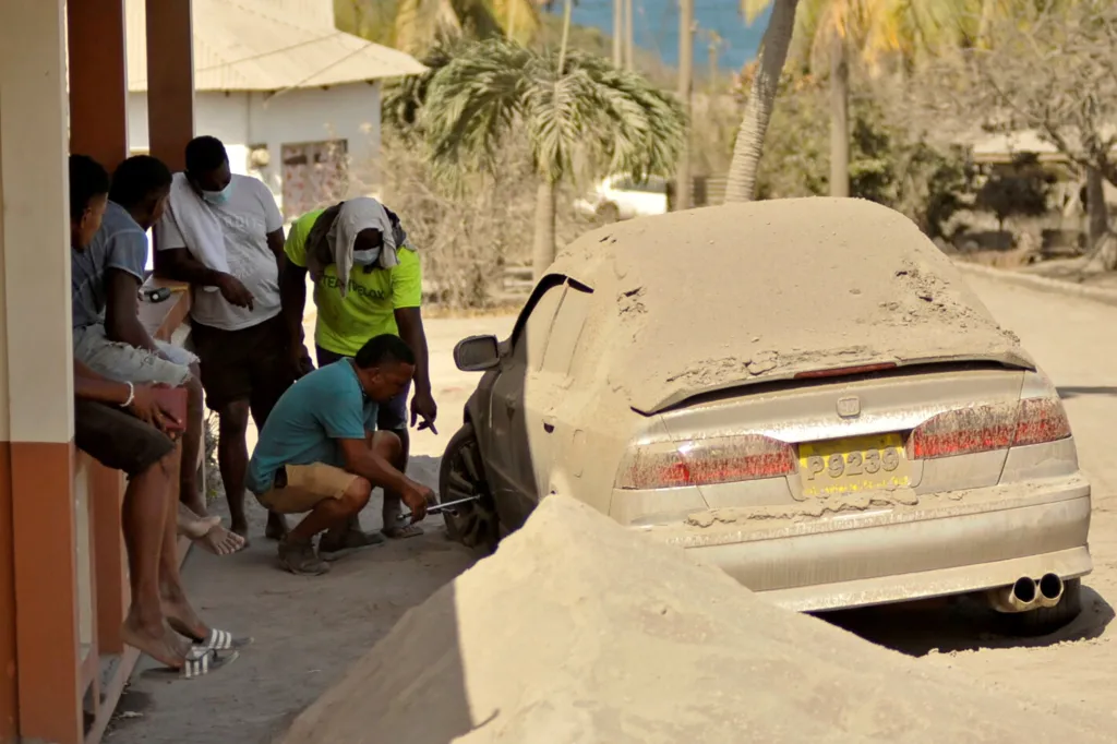 Muž na snímku opravuje defekt kola na svém autě, které je pokryté popelem po erupci vulkánu La Soufriere na Orange Hill (Pomerančový kopec), severní části ostrova Svatý Vincenc