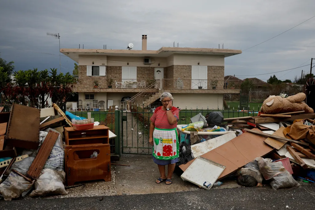 Starší žena stojí u svých věcí vyvezených ze zatopeného domu. Obyvatelé regionu se připravují na další silné deště