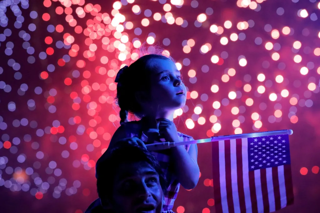 Dívka s americkou vlajkou sleduje ohňostroj během oslav 4. července