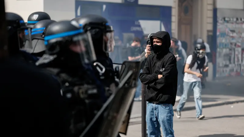 Demonstrant s kapucí a rouškou stojí vedle policistů během tradičního prvomájového pochodu odborů v Paříži