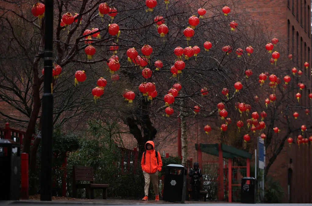 Muž se prochází pod stromy pokrytými červenými čínskými lucernami v britském Manchesteru