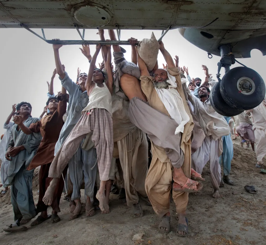 Lidé postižení povodní se snaží uniknout a skáčou na vrtulník, který 7. srpna 2010 přivezl potraviny do okreseu Muzaffargarh v provincii Paňdžáb v Pákistánu