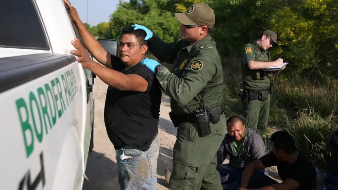 Pohraniční strážník prohledává a zatýká imigranty při jejich pokusu o ilegální přechod hranic z Mexika do USA v údolí Rio Grande