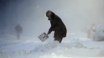 Žena s lopatou si prohrabává cestu ke svému autu ve sněhové bouři ve východním Bostonu.