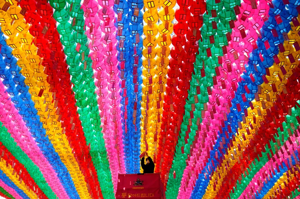 Pracovník s ochrannou maskou připojuje k lampionům modlitebními texty. Důvodem je příprava nadcházejících narozenin Buddhy. Vyfoceno v Soulu v Jižní Koreji