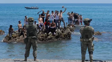 Maročané stojí na skalách před španělskými vojáky na pláži El Tarajal. Běženci z Afriky se snaží dostat do Evropy, migrační vlna se začala zvedat