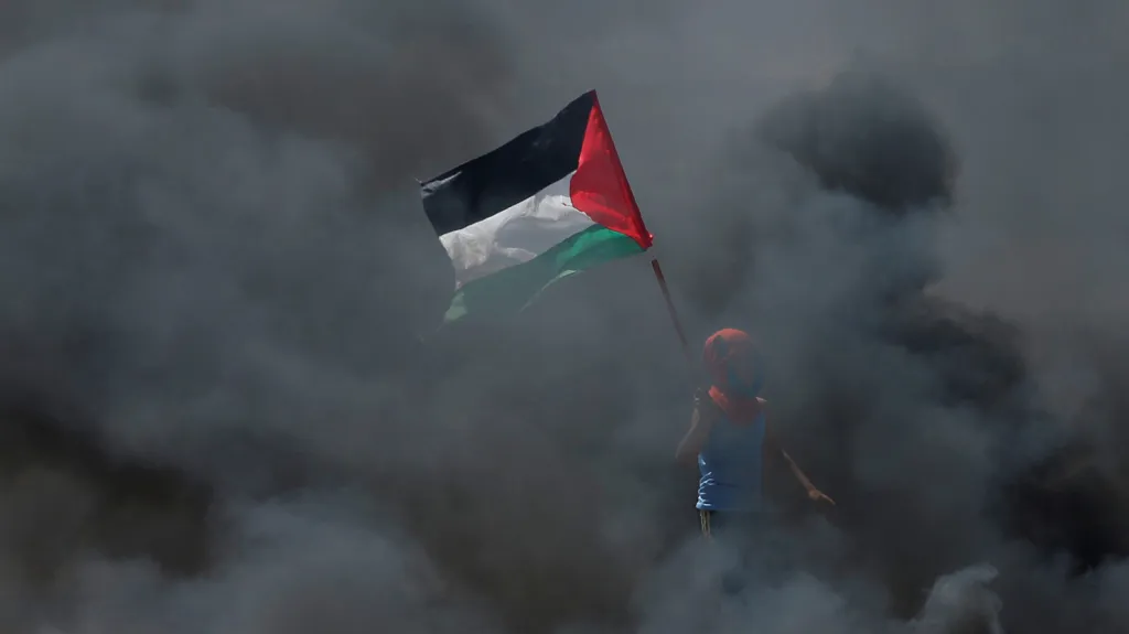 Chlapec s palestinskou vlajkou zahalen v dým z hořících pneumatik na barikádách během protestů nedaleko města Gaza