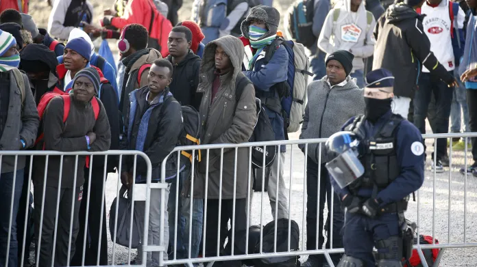 Nezletilí migranti v bývalém táboře u Calais čekají na autobus
