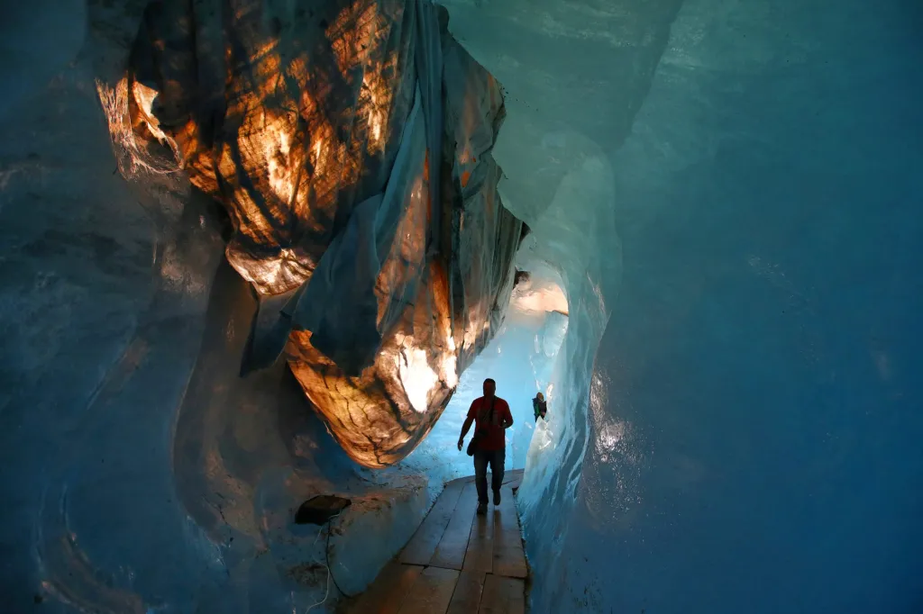 Lidé procházejí ledovou jeskyní pokrytou materiálem, který zabraňuje tání ledu, pod ledovcem Rhône ve Švýcarských Alpách u Furky v Obergoms. Ledovec se od roku 1879 zmenšil téměř o polovinu