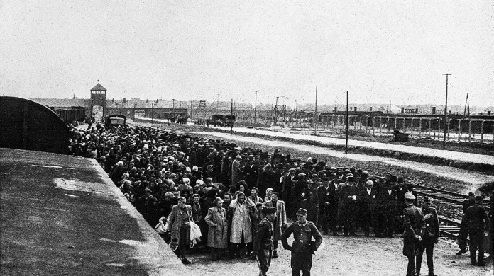 Před selekcí na rampě v Osvětimi-Birkenau, v pozadí je vidět táborová brána, kterou všechny vlaky přijížděly