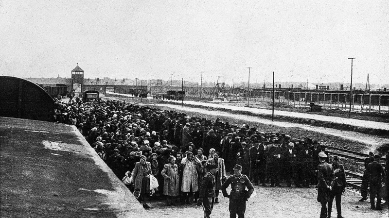 Před selekcí na rampě v Osvětimi-Birkenau, v pozadí je vidět táborová brána, kterou všechny vlaky přijížděly