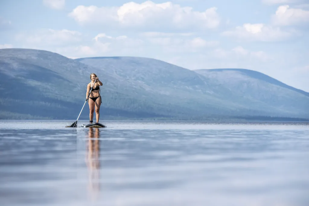 Žena užívající si na paddleboardu mimořádně teplého počasí na jezeře Pallasjarvi ve Finsku