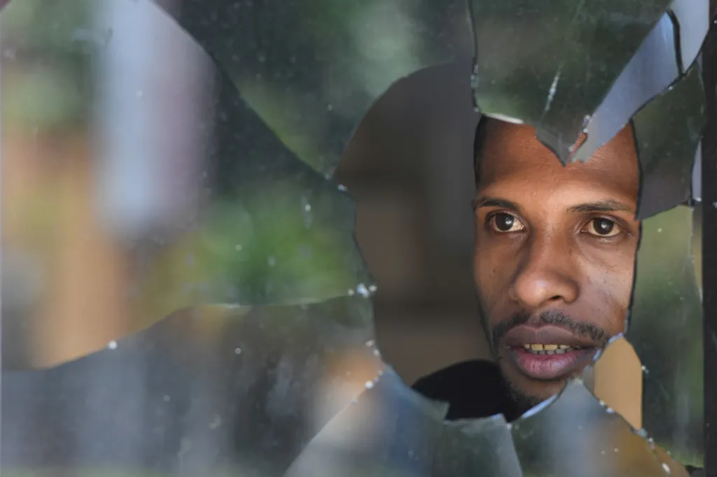 Skrz prostřelené okno sleduje muž situaci na ulici krátce po střelbě v indonéském Jayapuru