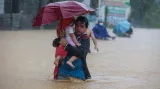 Muž nese dítě pod náporem deště na ulici ve filipínské provincii Rizal
