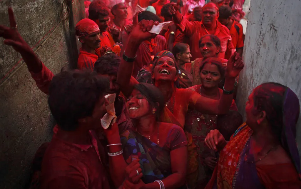 Lidé s tvářemi pokrytými barevným prachem tančí v ulicích během průvodu. Ten se koná devátý den desetidenního festivalu Ganest Chaturi v Mumbai, kdy lidé tancem a zpěvem doprovází modly ulicemi města až k řece, kam je poté rituálně ponoří. Mumbai, Indie, 2012