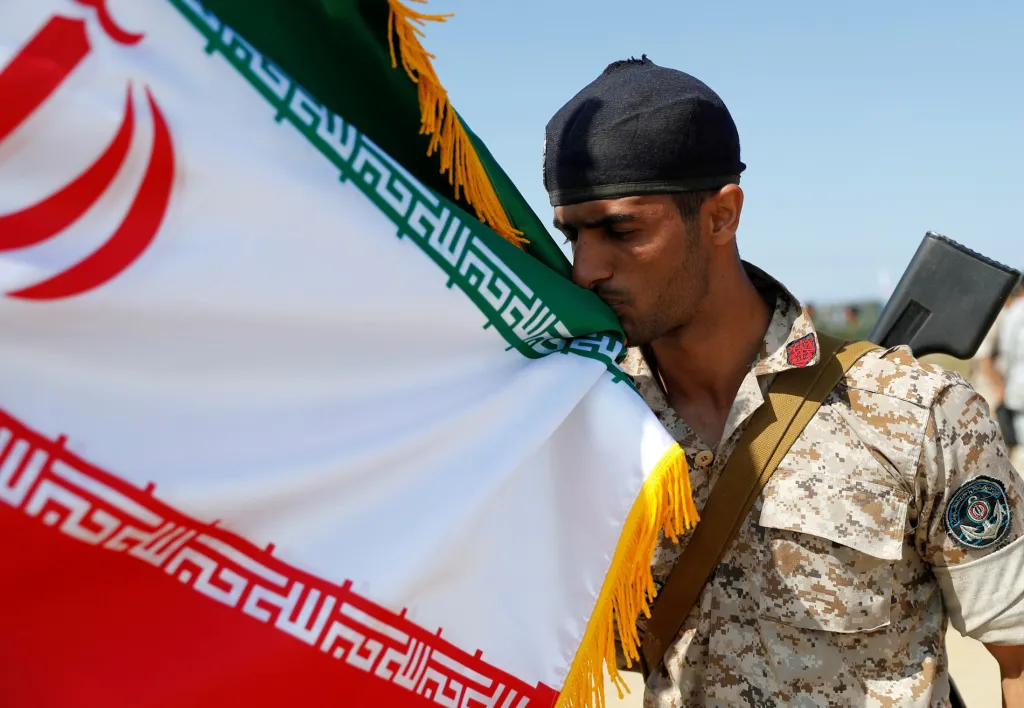 Příslušník íránských jednotek na břehu Baltského moře líbá vlajku jako akt pokory před státními symboly