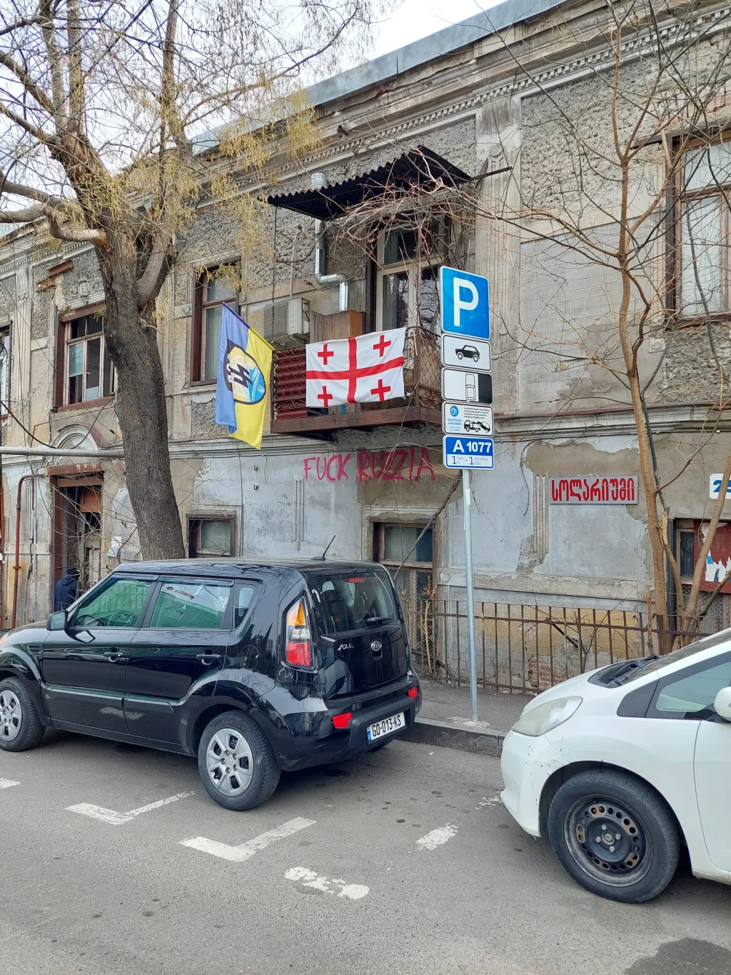 Vlajky Gruzie a pluku Azov, pod balkonem nápis „Je**t Rusko“