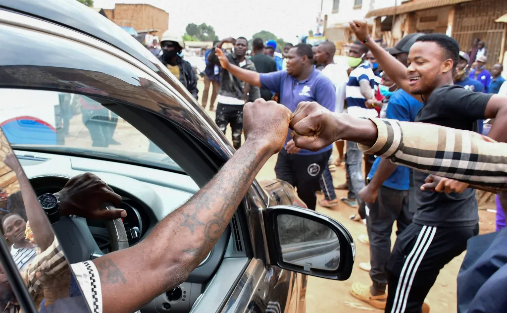 Uganďané volili prezidenta. V autě přijíždí jeden z kandidátů, zpěvák Robert Kyagulanyi Ssentamu, známý jako Bobi Wine, a zdraví příznivce.