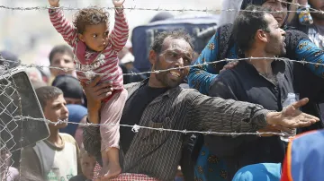 Syrský uprchlík s dítětem u hraničního plotu mezi Tureckem a Sýrií. Turecko střídavě uzavírá a otevírá hranice, aby regulovalo počty běženců ze sousední země. Do Turecka se tou dobou tlačí až 10 000 uprchlíků denně.
