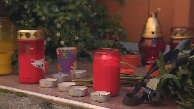 Lidé před dům pokládají květiny a zapalují svíčky