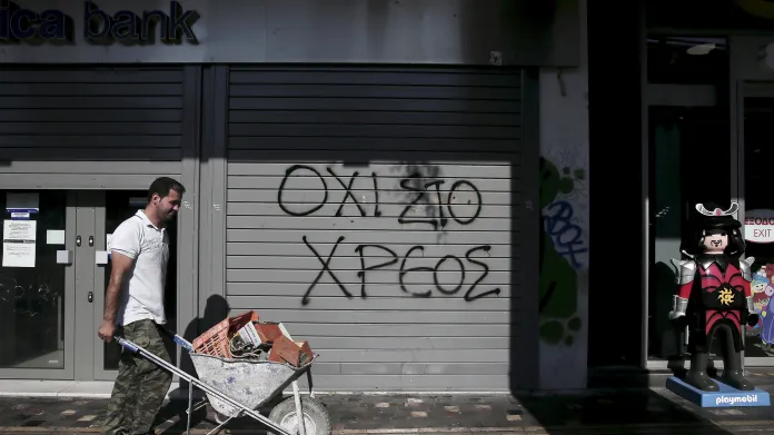 Muž veze kolečko aténskými ulicemi, v pozadí banka s graffiti: „Ne dluhu“