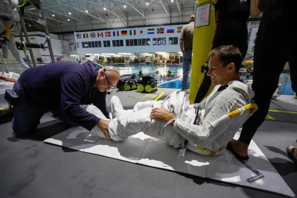 Astronaut Josh Cassada využívá pomoci kolegy, aby se dostal do skafandru